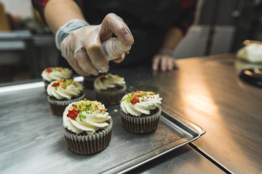 Kek dekorasyon süreci. Bir fırıncı bir tanesine şeker serperken ön planda bir sürü tatlı kek yakın çekim. Yüksek kalite fotoğraf