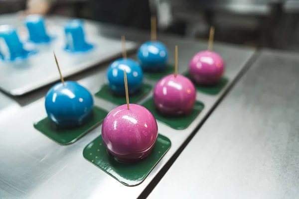 Pink and blue cakes with cocktail sticks placed on green square plates . Pink and blue cakes displayed on the metal kitchen counter. Blurred background. High quality photo