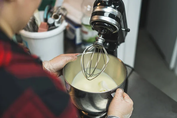 Home-cook concept. Unrecognizable caucasian person taking a bowl out of standing mixer with vanilla cream icing. High quality photo
