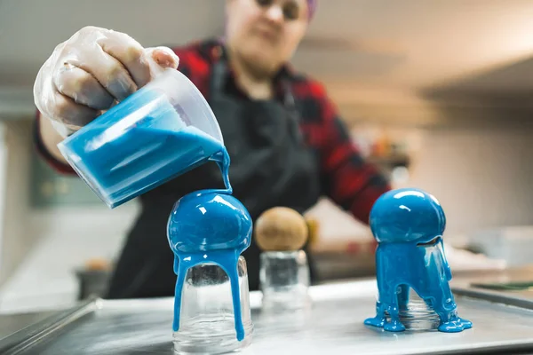 Pastry decorating. Unconventional icing with blue coloring. Pralines and sweets. Blurred pastry chef in the background. High quality photo