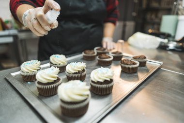 baker adding light blue sprinkles to the whipped cream cupcakes at the bakery, baking concept. High quality photo