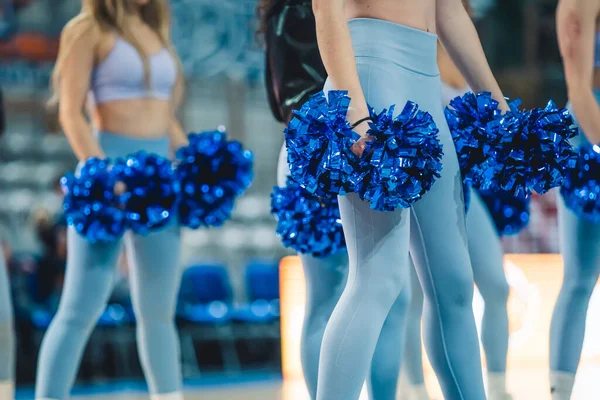 A group of cheerleaders are ready to perform. The cheerleaders are all wearing blue high-waisted tights. Holding pom-poms in their hands adds to the images energetic and celebratory atmosphere.