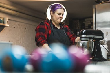 blurred shot of cookies on the front side and a female baker standing at the table and mixing products. High quality photo