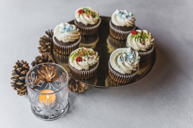 plate with chocolate cupcakes decorated for Christmas, pine cones and a glass with a candle, holiday mood. High quality photo