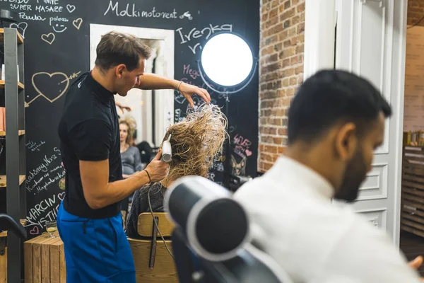blurred figure of a man at the salon and a hairdresser man drying clients hair backward. High quality photo