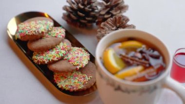 Sugar cookies covered halfway with colorful sprinkles standing next to winter tea with orange and cinnamon. High angle shot. High quality 4k footage