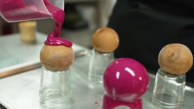 Decorating sweets. Unrecognizable caucasian person pouring magenta pink icing onto round cookies. High quality 4k footage