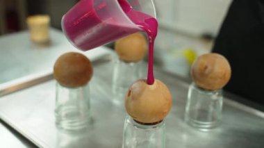 Decorating sweets. Unrecognizable caucasian person pouring magenta pink icing onto round cookies. High quality 4k footage
