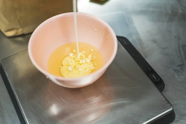 Baker pouring milk into oil in a bowl to prepare cupcake batter. Professional baking process. Wet ingredients. Horizontal indoor shot. High quality photo