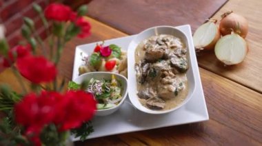 Traditional Polish dish - poledwiczki - tenderloin strips in mushroom sauce served with salad and potatoes. Blurred red flowers in the foreground. High quality 4k footage