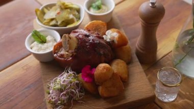 Oven-baked pork knuckle served on a wooden board along with source, potatoes and vegetables. Polish cuisine concept. High quality 4k footage