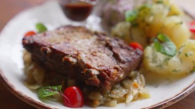 White plate with crispy pork ribs on braised cabbage along with dark sauce and boiled potatoes. Closeup portrait. Indoor shot. High quality 4k footage