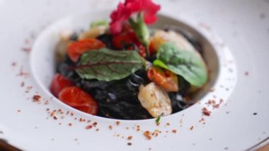 Top view of pasta dish. Black tagliolini pasta with prawns on white plate. Garlic and hot peppers for decoration. High quality 4k footage