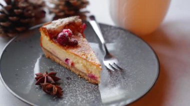 Piece of cherry cheesecake served on plate with powdered sugar and anise stars. Cup of hot tea. Pine cone decoration. Christmas baking. Festive dessert. Horizontal indoor shot. High quality 4k footage