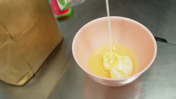 ベイカーはカップケーキ打者を準備するためにボウルに牛乳を油に注ぐ プロのベーキングプロセス 湿った成分 水平室内撮影 高品質4K映像 — ストック動画