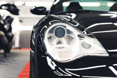 Moden sports car headlight. Shiny black car paint. Mechanic studio interior. Car detailing concept. High quality photo