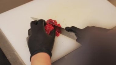 Chef in restaurant kitchen. Closeup portrait of beef tartare preparation. Person with sharp knife cutting beef on wooden board. High quality 4k footage