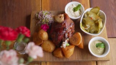 Top view of Golonka - oven-baked pork knuckle - traditional Polish dish served beautifully on a wooden board with oven-baked crispy potatoes, sauces, and pickles. High quality 4k footage