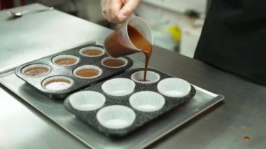 closeup view of female chef with gloves putting dough from a mug to paper cups for muffins. High quality 4k footage