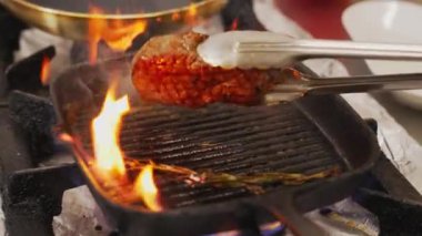 Frying process of striploin steak. Piece of medium rare piece of meat on grill frying pan in flames being turned over with metal cooking tongs. High quality 4k footage