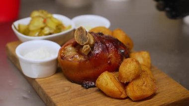 Meat dish in traditional Polish cuisine. Golonka z pieca - roasted pork knuckle with roasted potatoes, sauces, pickles and pepper shaker on wooden table. Top view. High quality 4k footage