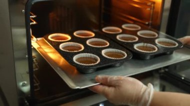 Person places tasty chocolate cupcakes on tray in a hot oven. Professional bakery and pastry making. High quality 4k footage