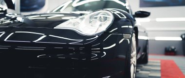 Front of sports car closeup. Indoor shot of black shiny sports vehicle during process of renovation and car detailing. High quality photo