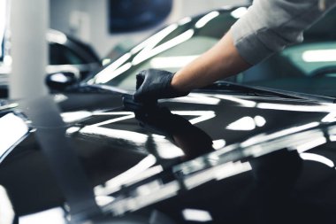 Closeup shot of black cars bonnet during application of ceramic layer by a professional car detailing studio worker. Shiny car. High quality photo