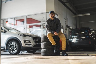 A man sitting on a stack of car wheels in a modern and well-equipped car repair shop. High-quality photo