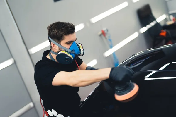 Car polishing service. Adult man in black t-shirt polishing black sports car varnish. High angle indoor shot. High quality photo