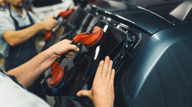 Close-up of two unrecognisable men holding rear window pane to install into back of car. Car maintenance. Garage work. Horizontal indoor shot. High quality photo