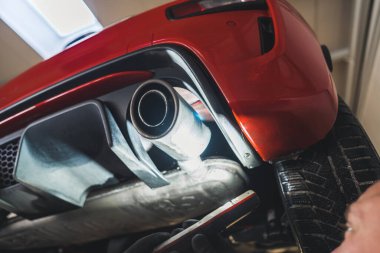 A close shot of a exhaust pipe and a red cars rear, Repair shop concept. High quality photo