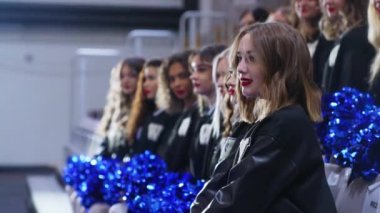 Five cheerleaders sitting down holding blue pom-poms and looking at the camera. Sport concept. High quality 4k footage