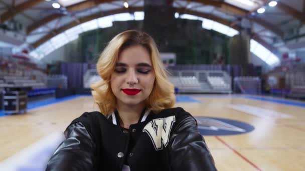 Blond Cheerleader Black Jacket Holding Ball Front Camera Blurred Foreground — Vídeo de Stock