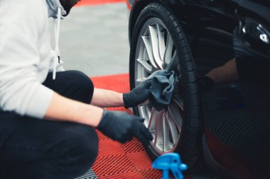 Unrecognisable man wearing black gloves crouched cleaning car wheel with a rag after blackening tires. Professional car detailing. Horizontal indoor shot. High quality photo