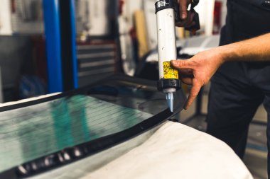 Close-up of man applying industrial adhesive to window pane before installing it into car. Garage work. Horizontal indoor shot. High quality photo