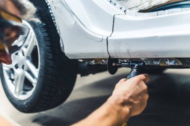 Man wearing protective goggles cutting out piece of body of car using small rotary saw. Garage work. Horizotal indoor close-up shot. High quality photo