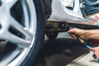 Unrecognisable man using small rotary saw tool to cut out part of body of car. Garage work. Horizontal indoor close-up shot. High quality photo