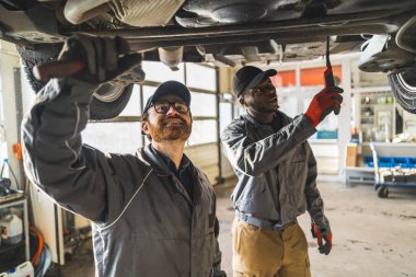 Medium shot of two mechanics working on a cars chassis and talking to each other. Repair shop concept. High quality photo