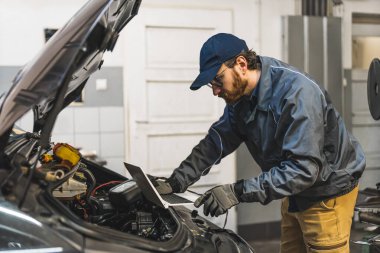 Skilled car mechanic repairing a car with the assistance of computer diagnostics. High-quality photo