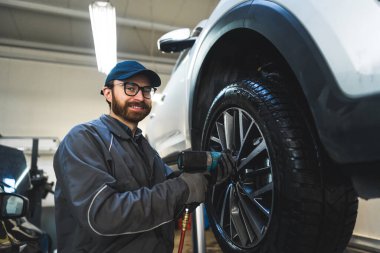 Low-angle shot of a smiling mechnic screwing a car wheel. Repair shop concept. High quality photo