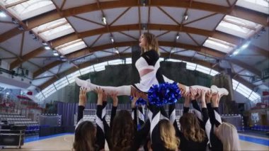 Dolly in of a cheerleading team with one cheerleader being held and doing a split. Sport concept. High quality 4k footage