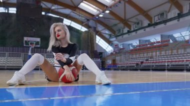 Cheerleader sitting on the floor with legs spread and a basketball between legs. High quality 4k footage