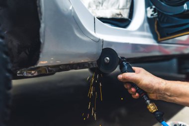 Close-up of male hand holding small rotary saw tool cutting out fragment of body of car. Garage work. Horizontal indoor shot. High quality photo