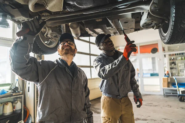 Two mechanics working under a lifted car using tools in a modern car repair shop. High-quality photo