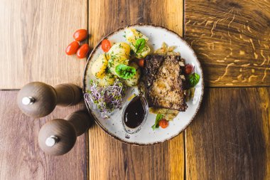 Top-down view of pork ribs with gravy boiled potatoes and radish sprouts served on white plate on rustic wood table. Polish cuisine. Horizontal indoor shot. High quality photo