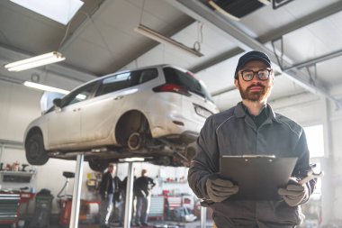Car mechanic with a clipboard in hand near a car on a lift for service and repair. High-quality photo