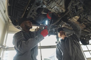 Two mechanics replacing the clutch of a lifted car using tools in an auto repair shop. High-quality photo