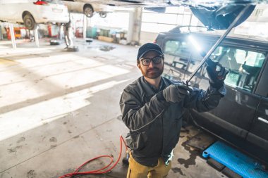 Mechanic with an LED light inspecting a car on a lift in a car repair station. High-quality photo