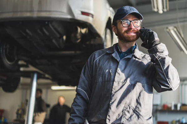 Car mechanic talking on the phone at an auto repair shop with lifted cars for repair. High-quality photo